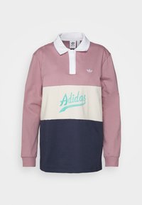 Langärmliges Poloshirt in Rosa, Creme und Marineblau. Merkmale einen weißen Kragen, das Adidas-Logo und ein Schriftlogo in Aquablau. Aus Baumwollmaterial.