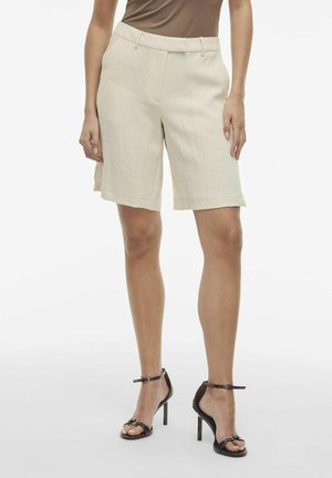Pantaloni corti di lino beige con una vestibilità rilassata, lunghezza fino a metà coscia, pieghe frontali e passanti per cintura. Abbinati a sandali neri con tacco alto e cinturini.