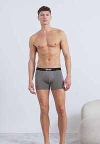 Γκρι ανδρικά εσώρουχα boxer με μαύρη μέση, που φέρουν το όνομα της μάρκας «BOSS» σε λευκό χρώμα. Το ύφασμα φαίνεται απαλό και εφαρμοστό.