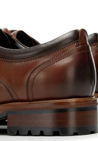 Brązowe skórzane buty o gładkim wykończeniu, okrągłym kształcie i kontrastującym ciemnym obcasie. Charakteryzują się wyraźnym przeszyciem i solidną, drewnianą podeszwą.