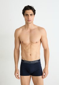 Donkerblauwe boxershorts van zacht materiaal, met een zwarte tailleband waarop het logo "TOMMY HILFIGER" centraal aan de voorkant is afgebeeld.