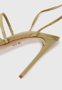 Sandale verte à talons hauts avec de fines brides, un bout pointu et une finition brillante. Un détail métallique près du talon rehausse le design.