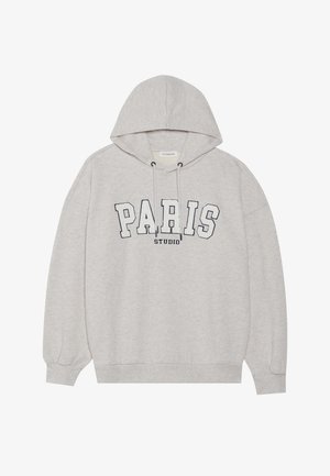 Siva dukserica od mekog materijala, s prednjim grafičkim natpisom "PARIS STUDIO" u podebljanim tamnoplavim slovima. Ima kapuljaču s špagom i rebraste manžete.