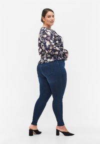 Blusa de color azul marino con estampado floral, de manga larga y cintura fruncida, combinada con jeans skinny de color azul oscuro y tacones negros de punta abierta.