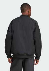 Casaco bomber preto feito de um tecido leve e texturizado. Punhos e bainha canelados. Apresenta um ajuste descontraído e uma superfície suave.