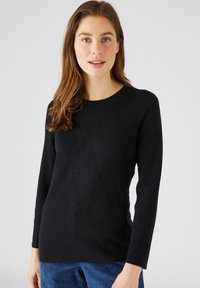 Suéter negro de punto acanalado con mangas largas y cuello redondo. Presenta un patrón texturizado con líneas diagonales en la parte delantera.