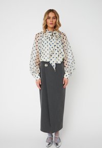 Blusa a pois in tessuto leggero, con fiocco e maniche a palloncino, abbinata a una gonna a involucro grigia e scarpe metalliche.