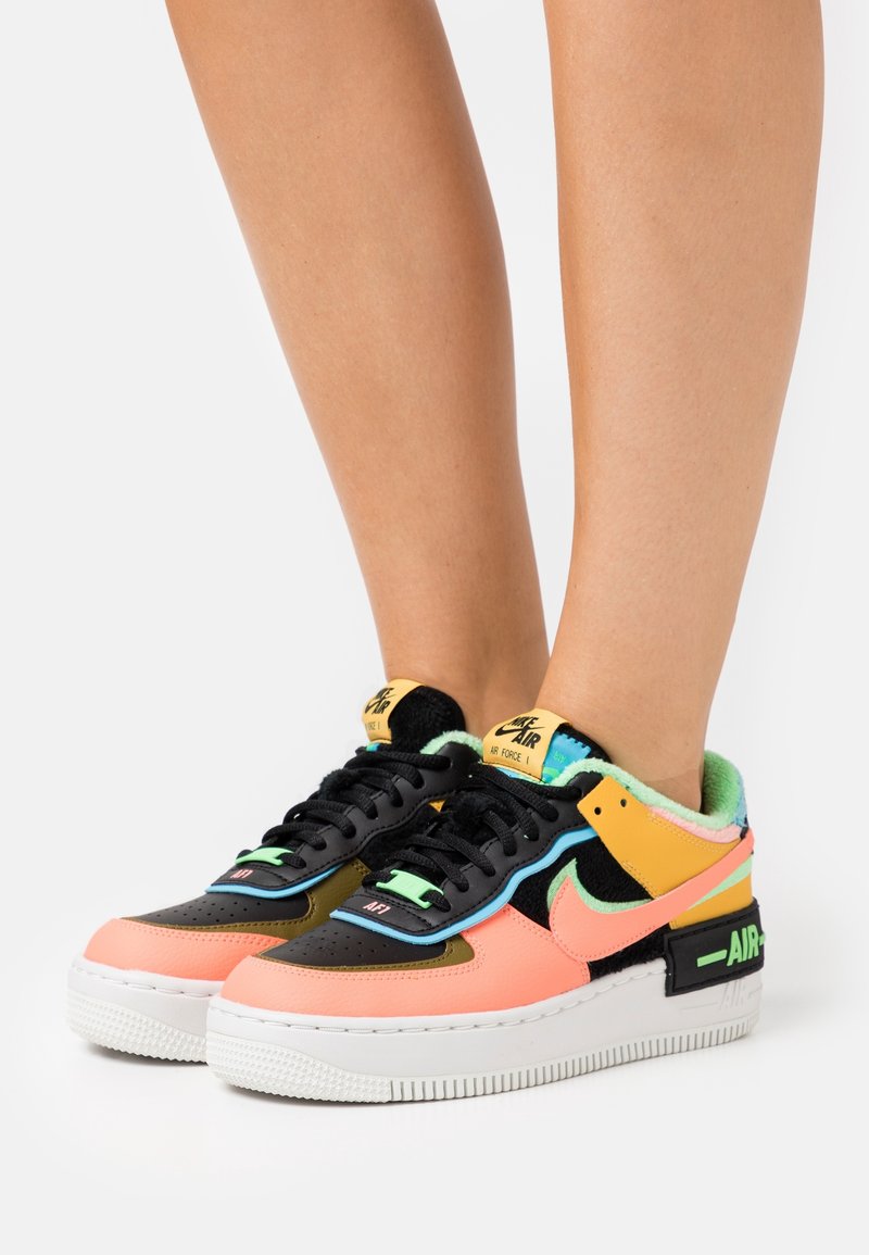 Colorful sneaker featuring a mix of black, peach, green, and yellow materials. Chunky white sole, textured accents, and branded tongue.