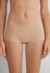 Bragas hipster para mujer en color beige, confeccionadas con una tela suave, que presentan un diseño sin costuras y un ligero brillo, con una pequeña etiqueta de logo en la banda elástica.