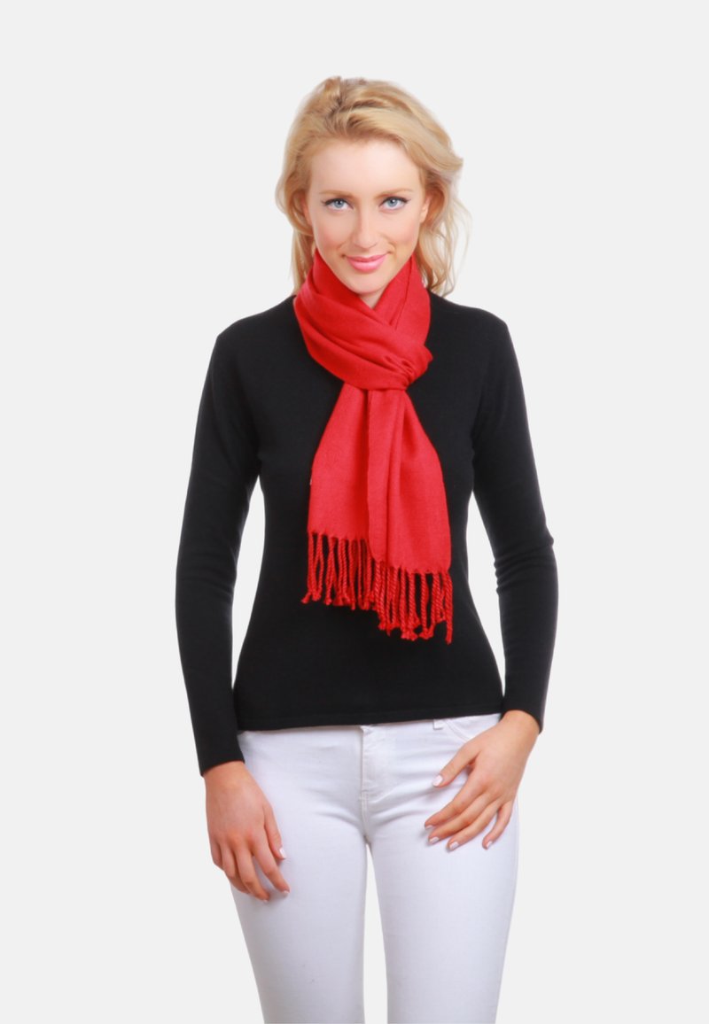 Écharpe rouge aux bords frangés, en tissu doux, drapée autour du cou. Le modèle porte un haut noir à manches longues et un pantalon blanc.