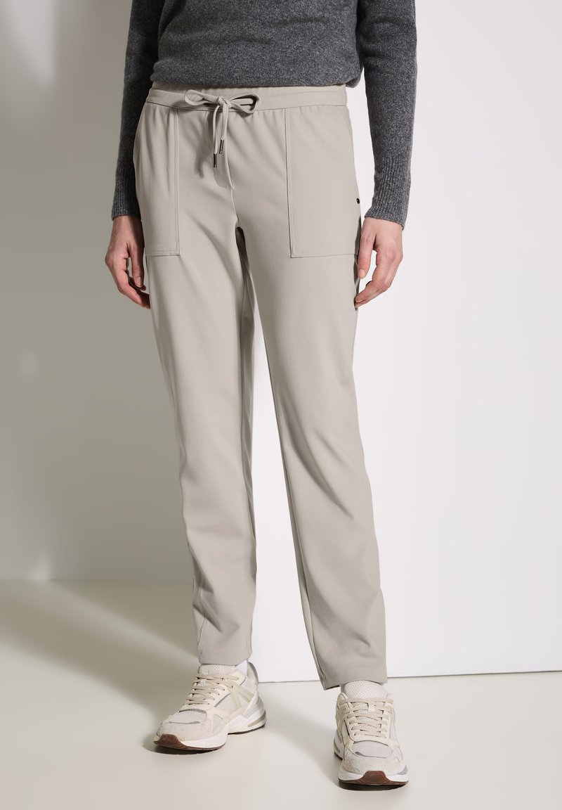 Ljust beige byxor med dragsko i midjan, med två framfickor, tillverkade av ett mjukt och lätt tyg. Bärs med ljusa sneakers.