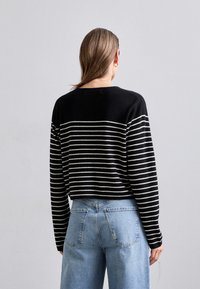 Černobíle pruhovaný svetr s kulatým výstřihem, volnější střih a žebrované manžety, spojený se světle modrými džíny s vysokým pasem.