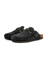 Sabots en suède noir avec une semelle en liège beige, dotés d'une sangle à boucle réglable et d'une texture lisse. Design de bout légèrement arrondi.