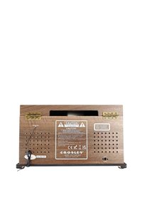 Altavoz de madera con acabado oscuro, que presenta una etiqueta de advertencia, orificios de ventilación de malla y bisagras metálicas. Incluye una entrada de alimentación y el logotipo de la marca.