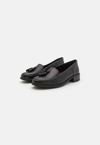 Pantofi loafers din piele neagră, cu toc mic bloc, prezentând un vârf rotund și un ciucure decorativ în față. Partea superioară texturată și finisaj neted.