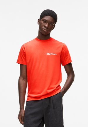 Piros rövid ujjú pamut póló, kerek nyakú, fehér nyomott logóval a mellkason. Vékony anyagú, testhez simuló fazon.