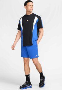 Męski strój sportowy składający się z czarno-niebieskiej, kolorowej koszulki z krótkim rękawem, niebieskich szortów oraz czarnych butów sportowych z niebieskimi akcentami.
