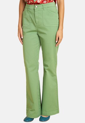 Green high-waist pants with front patch pockets worn with blue shoes and a red floral top, shown on a standing person.