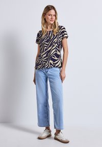 T-shirt a maniche corte blu navy con un motivo a strisce di zebra beige, abbinato a jeans a gamba larga azzurri e sneakers bianche.