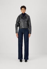 Hallhallagusse nahkjakk, millel on hall karvane krae, tõmblukuga taskud, kantud tummise turtlenecki ja siniste avarate pükstega, koos mustade saapadega.