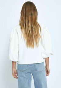 White linen blouse with puffed sleeves, paired with light blue high-waisted jeans. Smooth texture and minimalist design, no visible patterns.
