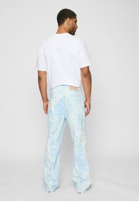 Light blue denim pants with a diamond pattern, worn with a white t-shirt. Straight-leg fit with a tag on the back waistband.