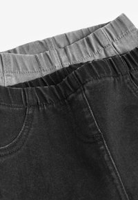 Pantalons avec taille élastique noir et gris, présentant une texture lisse, une coupe fuselée, deux poches et une couleur contrastante à la taille.