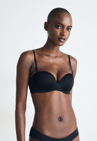 Soutien-gorge rembourré noir avec de fines bretelles ajustables, texture lisse et forme sans couture, conçu pour le soutien et le confort.