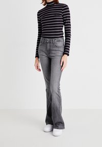 Jeans acampanados grises de cintura alta, con bolsillos frontales y un desvanecimiento sutil. Combinados con una camiseta de manga larga a rayas en blanco y negro.