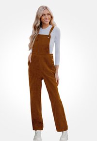 Jardinería de pana marrón con piernas anchas, tirantes ajustables, bolsillos laterales y detalles de botones. Combinado con una blusa de manga larga de color claro.