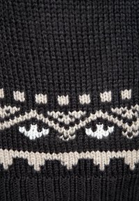 Czarny sweter dziany z geometrycznym wzorem w kolorze kremowym i białym. Wzór obejmuje stylizowane oczy oraz zygzakowate akcenty wzdłuż krawędzi.