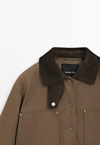 Giacca marrone con colletto in velluto a coste, bottoni a pressione e due tasche frontali. Realizzata in tessuto morbido con un design strutturato.