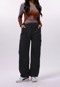 Haut marron et gris à manches longues avec design épaules dénudées ; pantalon cargo noir à jambes larges avec poches ; baskets blanches avec accents noirs.