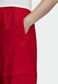 Röda, lätta shorts med en slät yta, elastisk midja, sidofickor och broderad Adidas-logotyp på vänster nederkant.