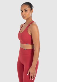 Sujetador deportivo rojo con tirantes anchos y leggings de tiro alto a juego, que presentan una tela suave y elástica y un diseño minimalista.