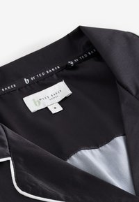 Fekete szatén ing sima textúrával és fehér szegéllyel a gallér mentén. Tartalmaz egy "b by Ted Baker" feliratú címkét, 8-as méretben.