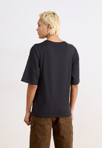 Tricou din bumbac negru, cu o croială lejeră, guler rotund și mâneci scurte, asociat cu pantaloni cargo maro cu imprimeu leopard.