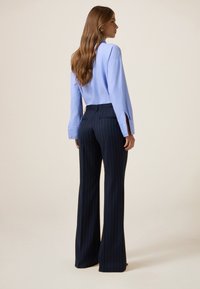 Camisa de botones de color azul claro con mangas largas y pantalones de pierna ancha a rayas navy, ambos con tejido suave y un corte entallado.