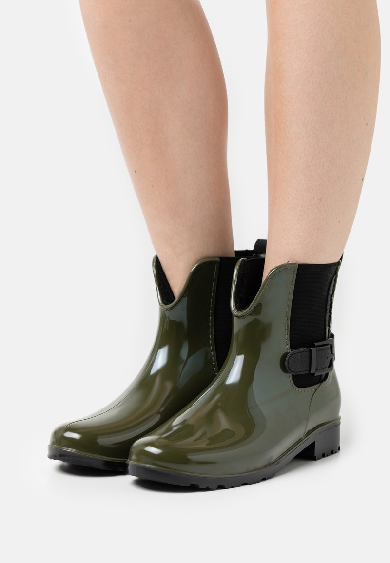 Bottes de pluie vertes brillantes avec un design élégant à hauteur de cheville, des panneaux élastiques sur les côtés et un détail décoratif de boucle sur le côté extérieur.