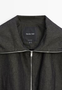 Donkergrijze jas met ritssluiting, brede kraag en zichtbaar merklabel "Massimo Dutti" aan de binnenkant van de halslijn.