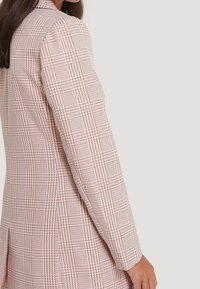 Blazer a cuadros en tonos rosa y blanco, con un corte entallado, tejido texturizado, mangas largas y aberturas laterales para mayor comodidad de movimiento.