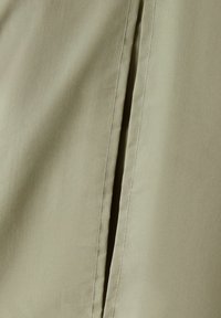 Světle olivově zelená látka se hladkým povrchem, která má detaily švu a jemný lesk. Žádné výrazné vzory nebo kovové prvky nejsou viditelné.