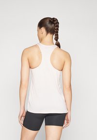 Lys rosa trenings tanktopp med racerback-design og ribbestruktur, kombinert med svarte tettsittende shorts. Glatt, mykt stoff med minimal detaljering.