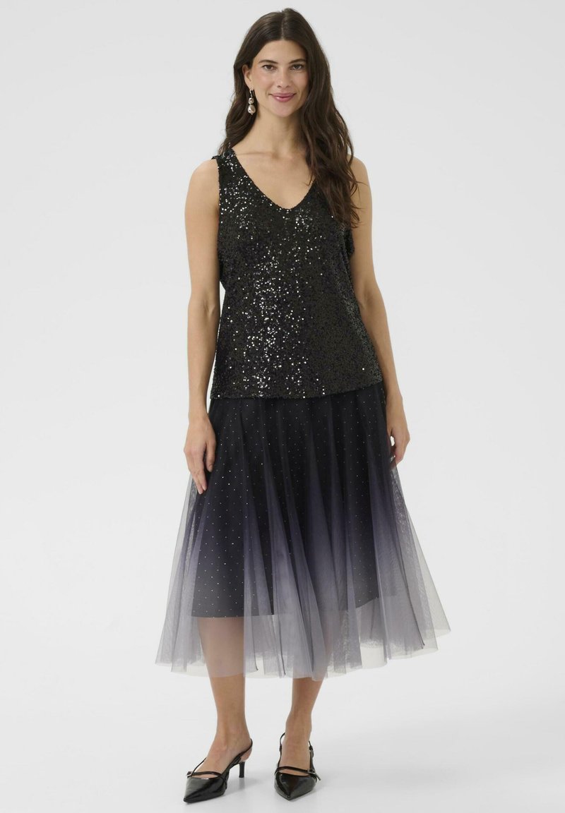 Černý flitrový top s výstřihem do V, spárovaný s dlouhou černou tylovou sukní s stříbrnými puntíky a černými botami na podpatku.