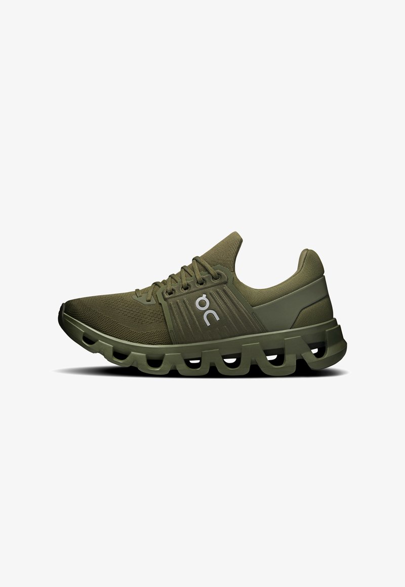 Chaussure de sport vert olive avec fermeture à lacets, tige en maille respirante et semelle coussinée présentant un design en vagues segmentées.