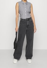 Grå jeans med vida ben kombinerade med en ärmlös, randig skjorta med knappar. Outfiten kompletteras med en svart väska och vita sneakers.