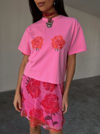 T-shirt in cotone rosa con due stampe di rose rosse sul davanti, sovrapposta a una gonna trasparente rosa decorata con motivi floreali.