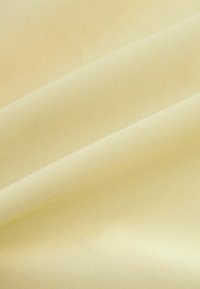 Tissu jaune clair avec une texture lisse et de subtils plis créant de douces ombres à la surface.