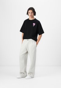 Svart bomull t-skjorte med oversized passform og rosa grafikk på brystet, kombinert med lys grå joggebukser og hvite sneakers.