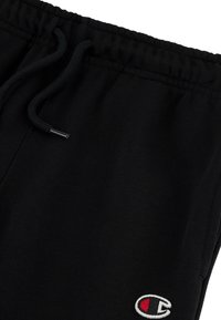 Pantaloni della tuta neri realizzati in misto cotone, con cintura elastica e cordoncino, e un logo ricamato bianco e rosso sul lato sinistro.